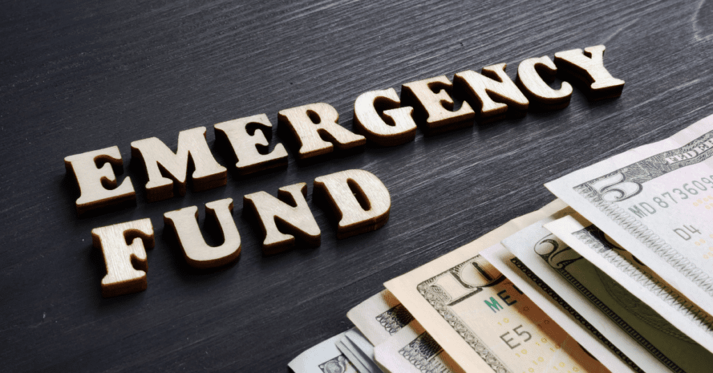 Wooden letters spelling out "EMERGENCY FUND" next to various currency notes on a dark wooden background.